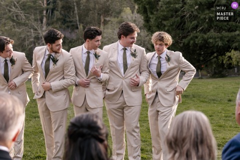 A humorous scene captured at a ceremony venue in Santa Barbara, Central Coast, as groomsmen, lined up in a row, pretend to have misplaced the bride's ring during the ceremony, all eyeing the last guy searching his pockets.