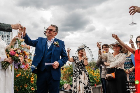 At London’s National Theatre, wedding guests enthusiastically clink glasses and cheer, marking the close of a heartfelt speech during the reception festivities.