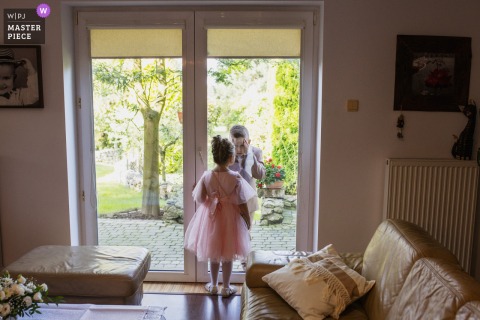 An endearing scene documented at the bride’s house in Krakow, Malopolskie, as a young boy gazes at a girl through glass door with pleading eyes, silently asking her to open the door, capturing a quiet moment of connection.