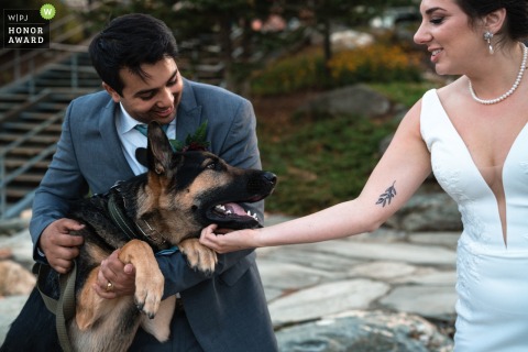 Outside at Sugarbush Resort in Vermont, the bride and groom play happily with their beloved dog, capturing a sweet moment together during their wedding celebrations.