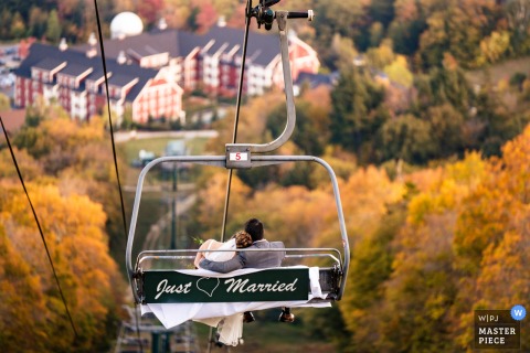 A scenic moment captured at Sugarbush Resort, Vermont, as the bride and groom ride a chairlift down from their ceremony. Photographed from another chair, the view beautifully documents vibrant fall foliage in the background.