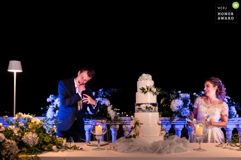 On a festive day in Trieste, Italy, the groom bites at the cap of a stubborn Prosecco bottle, bringing laughter and light heartedness to the scene.