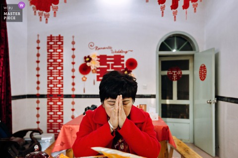 A serene moment captured at a home in Nanping, Fujian, as a mother, hands pressed together in prayer over her face, is beautifully documented with symmetrical framing, wishing for everything to go smoothly.