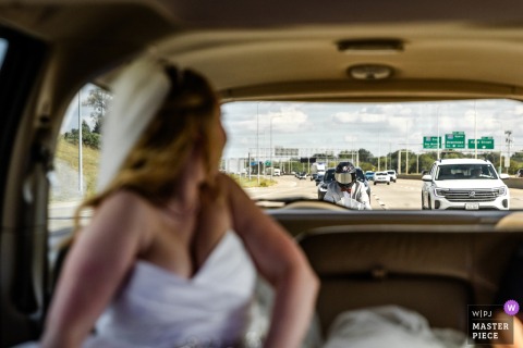 A joyful moment captured on Interstate 80 in Omaha, NE, as the bride, seated in the limousine’s backseat, realizes her man of honor on a motorcycle has caught up—beautifully documented.
