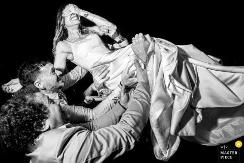 Friends Joyfully Lift The Bride In The Air At Hotel Colonial La Boulogne, Santa Fe, Argentina, Filling The Moment With Laughter. At Hotel Colonial La Boulogne in Santa Fe, Argentina, friends lift the bride above their heads with joyful energy, surrounding her with laughter and excitement on her wedding day.