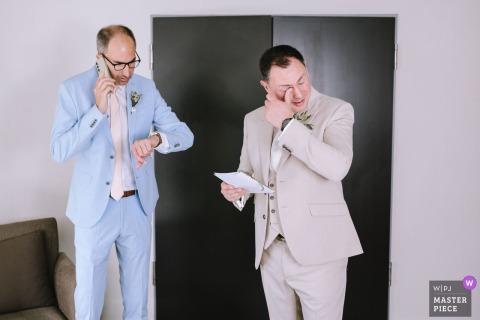 A Groomsman Takes A Phone Call While The Groom Weeps Over A Letter At Mercure Hotel, Krefeld, Germany. During a heartfelt moment at Mercure Hotel in Krefeld, Germany, a groomsman answers a phone call while the groom weeps, reading a touching letter from his wife.