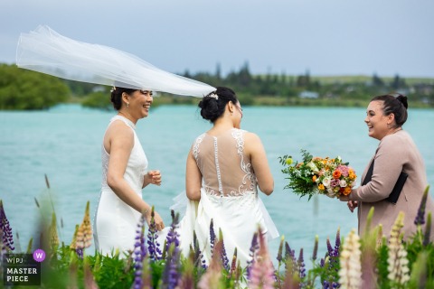Wind Lifts Weiwei’s Veil At Lake Tekapo, New Zealand, Creating Drama Just As The Elopement Ceremony Is Set To Begin. The wind picks up Weiwei’s veil at Lake Tekapo, New Zealand, just as the elopement ceremony is set to begin, adding drama and movement to the mountainside moment.