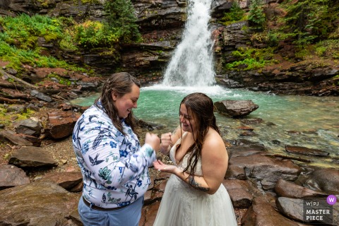 In The Rain Beside A Waterfall In Silverton, Colorado, The Couple Settles Vows Order With Rock, Paper, Scissors. At a waterfall in Silverton, Colorado, the wedding couple plays a spontaneous game of rock, paper, scissors in the pouring rain to decide who will recite vows first.