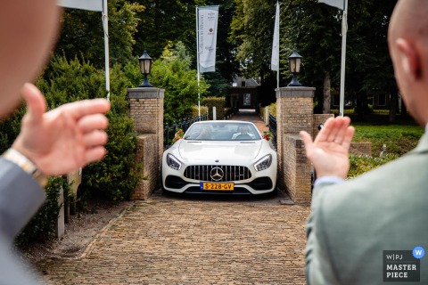 Guests In Noord Brabant Excitedly Welcome The Arriving Couple And Their Big Car At The Small Gated Reception Venue. Excitement buzzes as the couple arrives in a big car at the small gated reception venue in Noord Brabant, welcomed by eager guests ready to celebrate their big day.