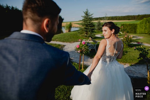 In Budapest, at the ceremony location, a bride leads her partner forward with a gentle smile, glancing back as they step into a new chapter of their journey together.