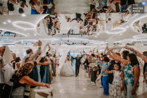 In Giardino Del Mago, Guests Wave Napkins For The Newlyweds, Creating A Festive And Welcoming Atmosphere At The Reception. Cheers erupt at Giardino del Mago as guests wave napkins in the air, warmly welcoming the newlyweds upon their festive arrival at the mirrored reception venue.
