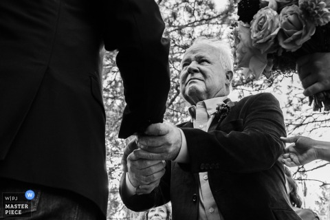   At Grizzley Gardens in Montana, a teary-eyed father of the bride shares a heartfelt handshake with the groom before lovingly handing his daughter over at the altar.