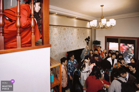   From her home in Nanping, Fujian, the bride peers through the railing, watching guests play lighthearted games in the attic as she awaits the next part of the ceremony.