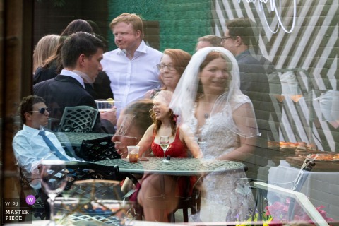   Multiple reflections merge in a single exposure at Baldoria on the Water in Lakewood, Colorado, as the bride and her wedding guests appear together in a beautifully artistic scene.