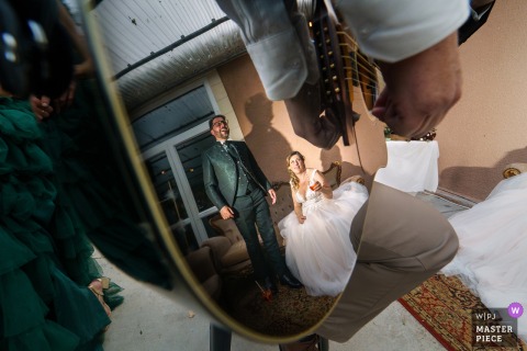 A Creative Reflection At Château Caillivet In Gironde, France Shows The Couple In Their Friend’s Guitar During Cocktail Hour. A creative scene at Château Caillivet in Gironde, France shows the couple reflected in their best friend’s guitar while he plays a song for them during the cocktail hour.