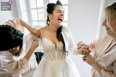   Laughter fills the air at Domaine de la Chartrognière, as the bride bursts out laughing while her bridesmaid struggles with removing a stubborn label from the bride’s wedding coat.