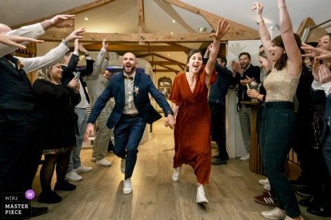   At Le Clos de Florie in Porte-de-Savoie, Savoie, the bride and groom make a lively and festive entrance before dinner, greeted by enthusiastic friends and family.