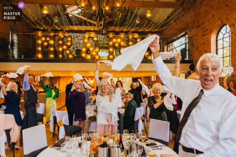   Guests exuberantly wave napkins in the air at The Carriage Hall, marking the couple’s grand entrance and filling the room with energy and anticipation for the evening ahead.
