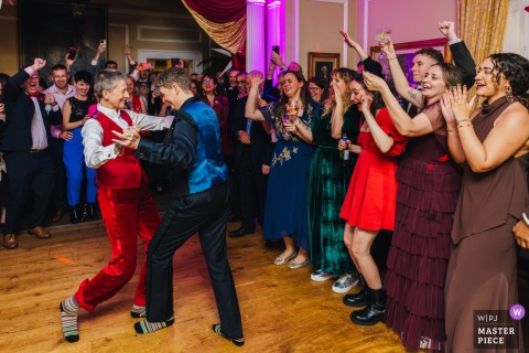 The Couple’s First Dance In Socks At Langar Hall Brings Raised Hands, Cheers, And A Lighthearted Atmosphere. The couple shares their first dance in socks at Langar Hall, as guests raise their hands and cheer, celebrating the fun and carefree atmosphere of the moment.