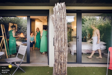   At the reception venue during getting ready, the left side of the room buzzes with bridesmaids getting ready while, on the right, the groom steps out of the shower with only a towel for company.