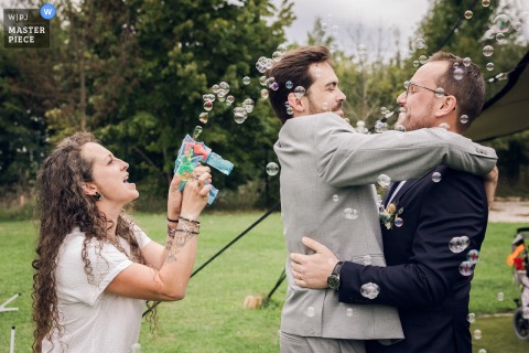   The end of the ceremony brings a playful scene as a relative kisses the groom while another guest fires a bubble gun, sparking laughter among family and friends.