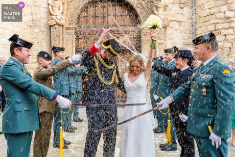   The couple walks beneath raised swords at Iglesia de San Ildefonso in Jaén, Spain, with rice falling like confetti, blending military tradition and exuberant celebration.