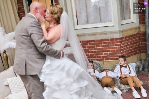 In Noord Holland, children at the ceremony location peek and hide as the couple shares their official kiss, bringing shy smiles and gentle humor to the special moment.