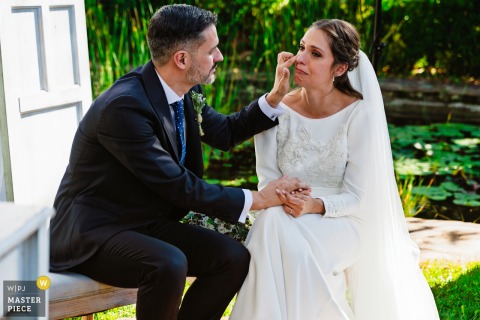   Seated together outside at Hacienda La Masía in Linares, Jaén, Spain, the groom gently wipes tears from the bride’s face in a peaceful, intimate scene away from the main festivities.