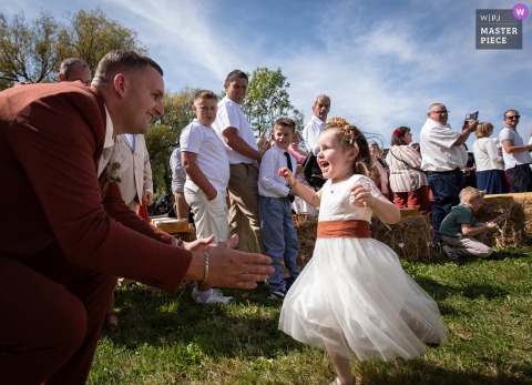 Groom Kneels To Warmly Greet His Daughter Just Before Bride Arrives At The Brittany Wedding Location. At the ceremony location in Brittany, the groom kneels down to welcome his young daughter warmly, sharing a special greeting before the bride arrives for the wedding.