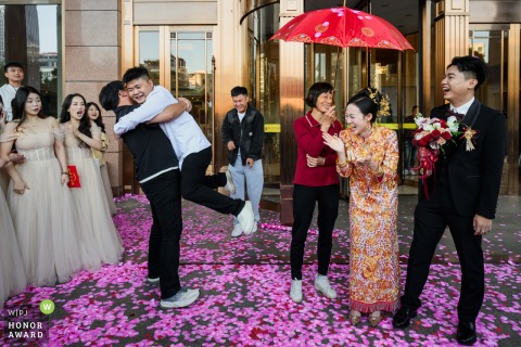 Best Man Joins Playful Pick-Up-The-Bride Game, Bringing Laughter To The Wedding Celebration At A Hotel In Guangdong At a hotel celebration, the bride and groom look on as the best man enthusiastically joins the playful game of picking up the bride, offering laughter and excitement in Guangdong.