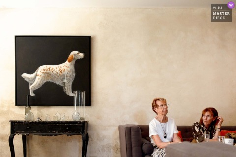 Women Relax Near A Dog Painting At Domaine Des Patras, France, Blending Art And Friendship At The Wedding. At Domaine des Patras, France, a playful scene unfolds as a group of women rest near a painting of a dog, blending art and camaraderie during the wedding celebration.