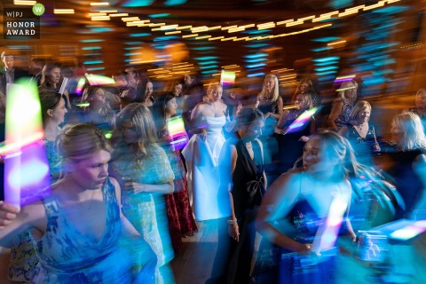 On the vibrant dance floor at Evergreen Lake House in Colorado, the bride stands framed by swirling colors and energy, embracing celebration at this party venue.