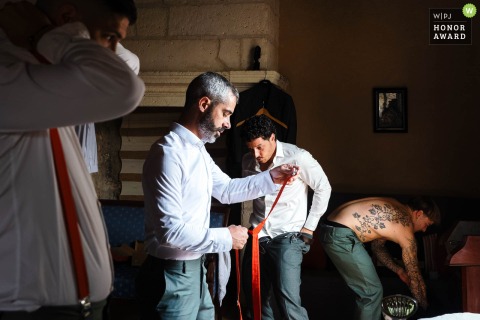 Men Prepare Together In Sunlit Room At Family Home In Brantôme, Dordogne, Sharing Quiet, Intimate PreWedding Moments At a family home in Brantôme, final touches are made as several men prepare together in a sunlit room, sharing a quiet, intimate moment.