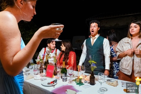 Surprise Follows A Wine Spill At A Brantôme Family Home, As The Groom Watches His Witness’s Mishap. At a family home in Brantôme, the groom looks on in surprise as a witness accidentally spills wine across the table and onto her dress, while a friend silently judges the mishap.