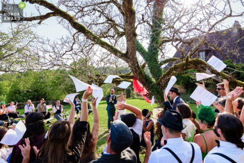 At Parc De La Fage In Journiac, Dordogne, Guests Toss Lyric Sheets To Congratulate Newlyweds After A Group Song Ending a group song at Parc de la Fage in Journiac, Dordogne, guests joyfully toss lyric sheets into the air, congratulating the newlyweds at the outdoor venue.