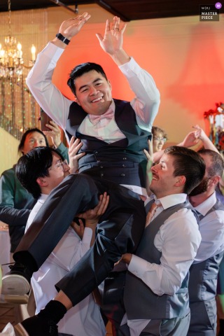 Joyful Cheers Fill Troutdale House In Oregon As Friends Hoist The Groom, Celebrating His Wedding With Laughter. Cheers ring out at Troutdale House Wedding Venue in Oregon as the groom is hoisted into the air by his friends, surrounded by laughter and celebration.