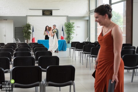 At the Frouzins Town Hall wedding venue in Haute-Garonne, the bride's daughter exits the room laughing, while the couple embrace behind her near the altar.