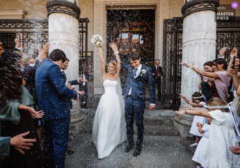 Just Married In Crocetta, Turin, The Couple Walks Through Confetti, Surrounded By Family And Friends’ Excitement. Moments after exchanging vows in Crocetta, Turin, the bride and groom walk together as they’re showered with confetti, surrounded by the exuberance of family and friends.