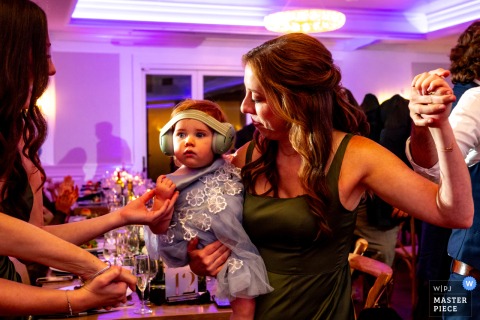   On the dance floor in Fredon Township, NJ, a woman balances joy and parenthood as she dances while lovingly holding her baby during the lively wedding celebration.