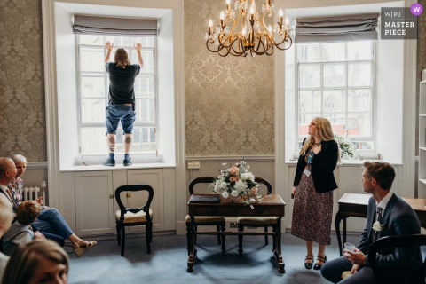 A Quick Pause Refreshes All As The Caretaker Opens A Window During The Guildhall Wedding In Bath, Somerset. A wedding ceremony at The Guildhall in Bath comes to a brief pause as the caretaker steps in to open a window, giving everyone a chance to catch their breath.