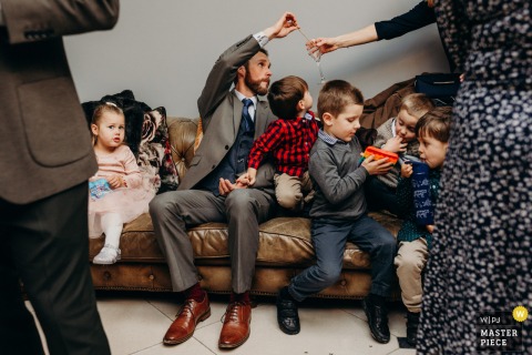 A Cozy Family Moment On The Sofa Unfolds During The Reception At Charlton House In Shepton Mallet, Somerset. Kids and their dad share a quiet, cozy moment on a sofa during the wedding reception at Charlton House in Shepton Mallet, enjoying some downtime amidst the festivities.