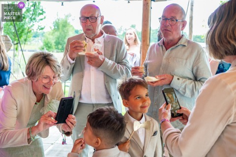   During the reception at Breeze, both grandmothers eagerly take photos of the children while the grandfathers sit back and enjoy their cake, blending family fun with sweet treats.