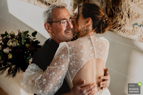 A Father Shares An Emotional Hug Seeing His Daughter In Her Dress At Château De Denonville, France, Reception Venue Inside Château de Denonville, France, a father embraces an emotional moment with his daughter as he sees her in her wedding dress at the reception venue.