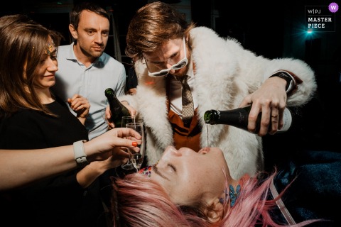 High Spirits At Château De Denonville, France As Guests Pour Champagne For Each Other Awaiting Their Own Taste. The celebration heats up at Château de Denonville, France, where guests enthusiastically pour champagne into each other’s mouths while others eagerly wait with glasses in hand for a taste.