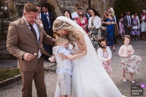   Relaxed happiness at Danby Castle in North Yorkshire as the bride warmly embraces the couple's son following their ceremony, surrounded by loved ones.