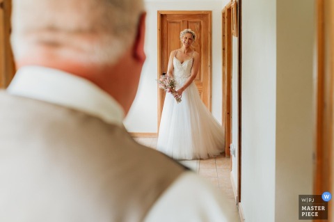   A bright hallway at a private farm in Dorset, UK, sets the scene as the father of the bride sees his daughter in her wedding dress for the very first time.
