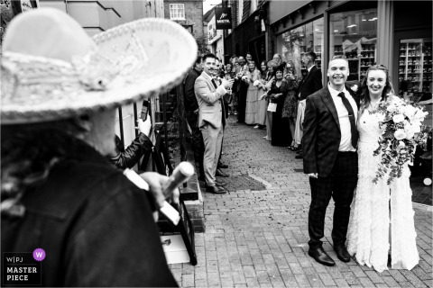 A Sombrero-Clad Busker Serenades The Couple With Festival Spirit At St Albans Museum & Gallery In Hertfordshire. Sombrero-wearing busker serenades the bride and groom at St Albans Museum & Gallery in Hertfordshire, surrounding the couple with laughter, music, and festive energy.