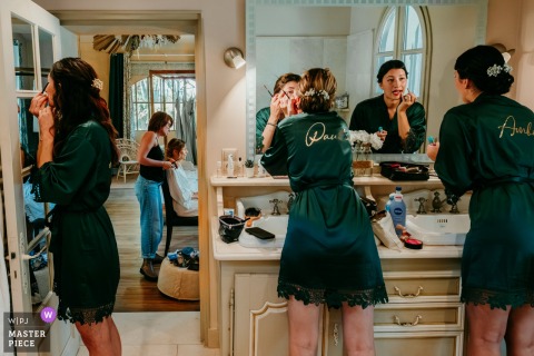   Bridesmaids gather in the bathroom to apply makeup together at Domaine du petit Malherbes, while the bride has her makeup done in the next room, adding to the excitement of getting ready.