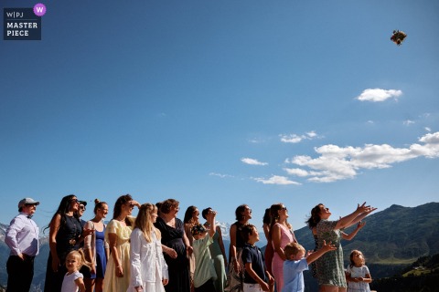 Cocktail Hour In Fribourg, Switzerland Draws A Crowd As Guests Compete For The Bride’s Bouquet Under A Blue Sky. In Fribourg, friends and family eagerly gather outside under a blue sky for the bride's bouquet toss during cocktail hour, creating a lively scene as everyone vies for the prize at the reception.