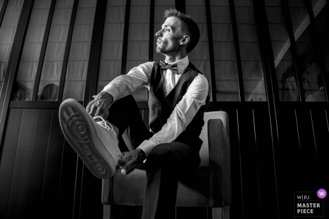Alone At Château Des Girards In France, The Groom Adjusts His Attire Before Greeting Loved Ones On Wedding Day. The groom all alone, completes his preparations at Château des Girards in France, adjusting his attire and readying himself before heading out to greet loved ones on his wedding day.